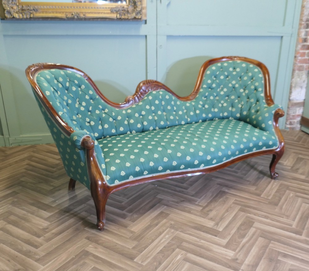A Victorian double spoon-back settee featuring a polished mahogany frame with deep-buttoned green patterned fabric upholstery.