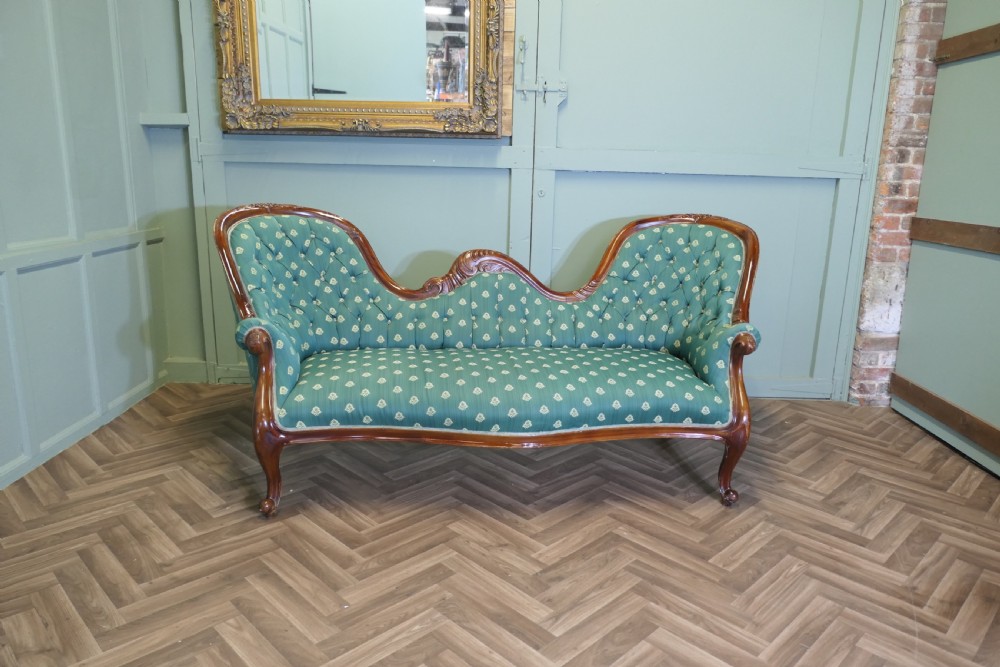 A Victorian double spoon-back settee featuring a polished mahogany frame with deep-buttoned green patterned fabric upholstery. View II
