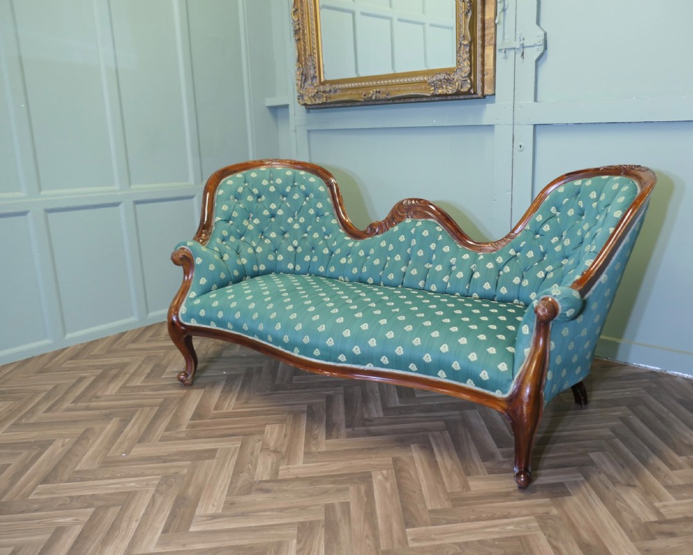 A Victorian double spoon-back settee featuring a polished mahogany frame with deep-buttoned green patterned fabric upholstery. View III