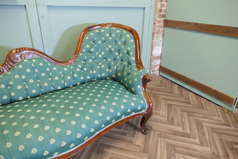 A Victorian double spoon-back settee featuring a polished mahogany frame with deep-buttoned green patterned fabric upholstery. View VI