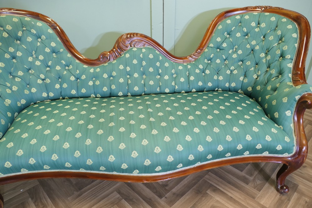 A Victorian double spoon-back settee featuring a polished mahogany frame with deep-buttoned green patterned fabric upholstery. View VIII