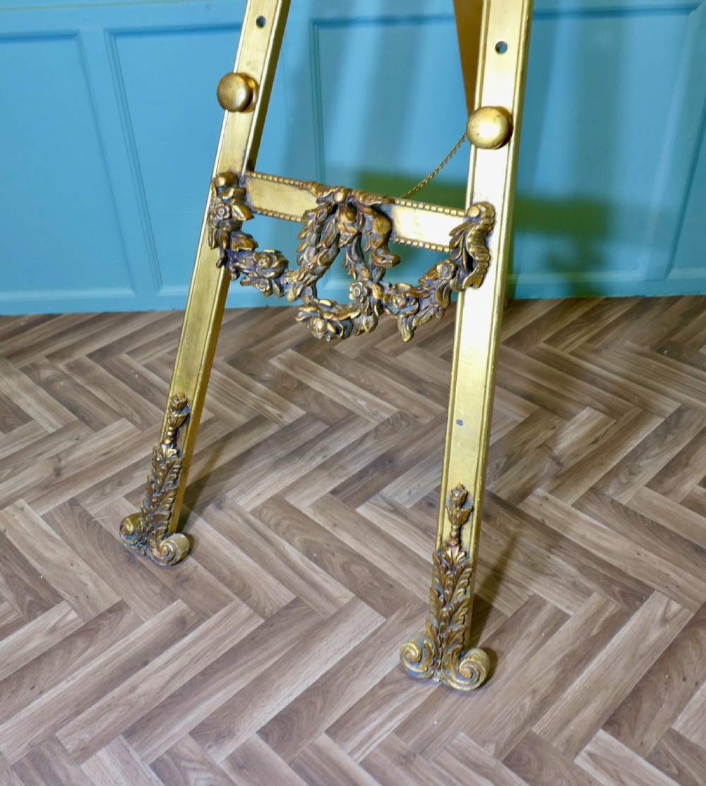A tall French carved giltwood floor easel featuring floral swags, a top cresting motif, and scrolled feet. View VI
