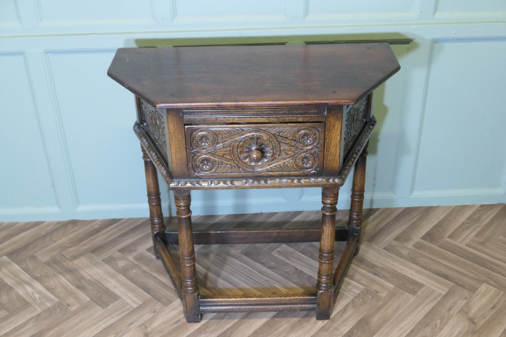A dark oak credence table featuring a canted top, a single relief-carved drawer, turned legs, and a lower stretcher base. View II