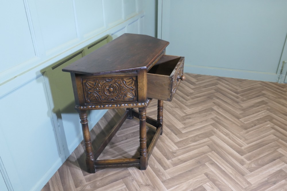 A dark oak credence table featuring a canted top, a single relief-carved drawer, turned legs, and a lower stretcher base. View IV