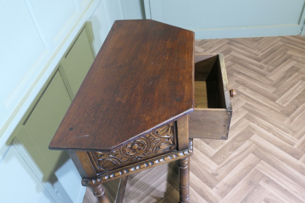 A dark oak credence table featuring a canted top, a single relief-carved drawer, turned legs, and a lower stretcher base. View V