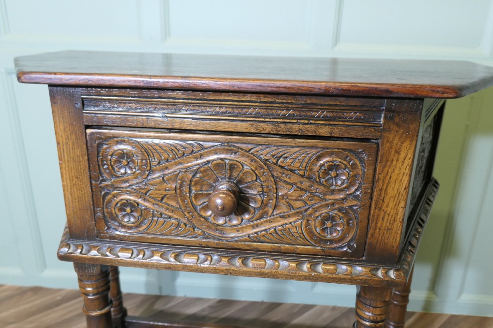 A dark oak credence table featuring a canted top, a single relief-carved drawer, turned legs, and a lower stretcher base. View VI