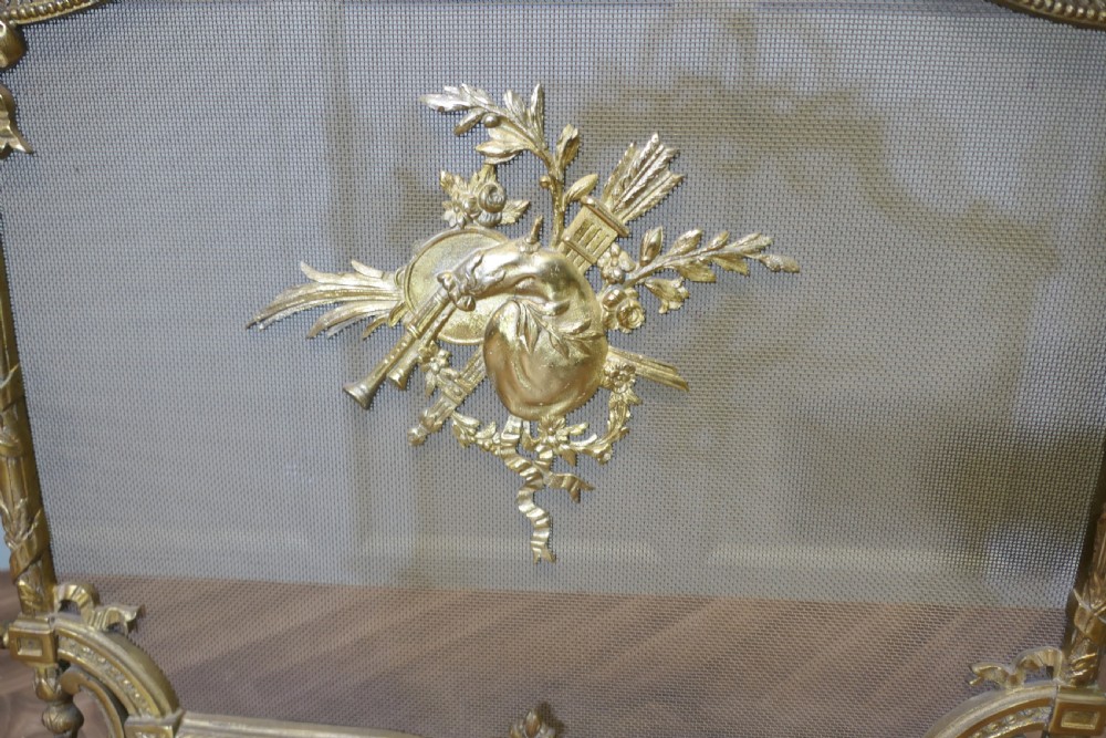 An ornate French gilded brass fire screen featuring intricate floral swags, a central bow motif, fine mesh panel, and decorative cabriole feet. View III