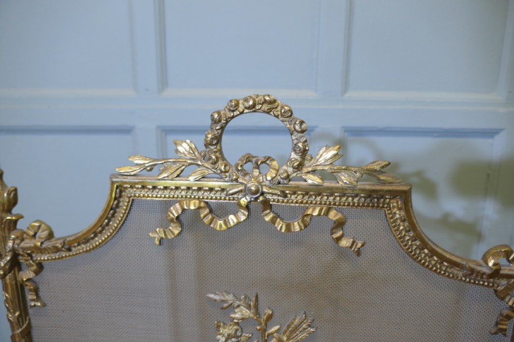 An ornate French gilded brass fire screen featuring intricate floral swags, a central bow motif, fine mesh panel, and decorative cabriole feet. View V