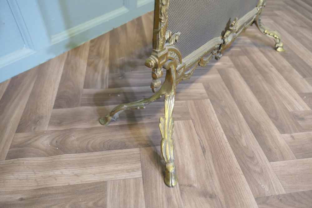 An ornate French gilded brass fire screen featuring intricate floral swags, a central bow motif, fine mesh panel, and decorative cabriole feet. View VI
