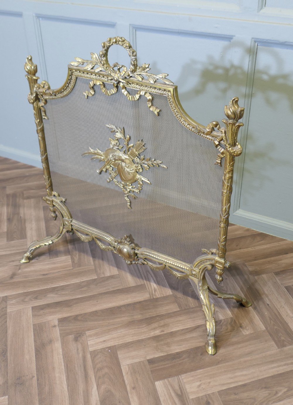 An ornate French gilded brass fire screen featuring intricate floral swags, a central bow motif, fine mesh panel, and decorative cabriole feet. View VII