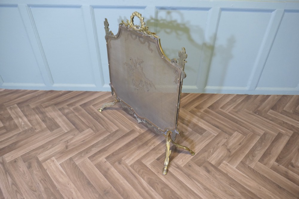 An ornate French gilded brass fire screen featuring intricate floral swags, a central bow motif, fine mesh panel, and decorative cabriole feet. View IX