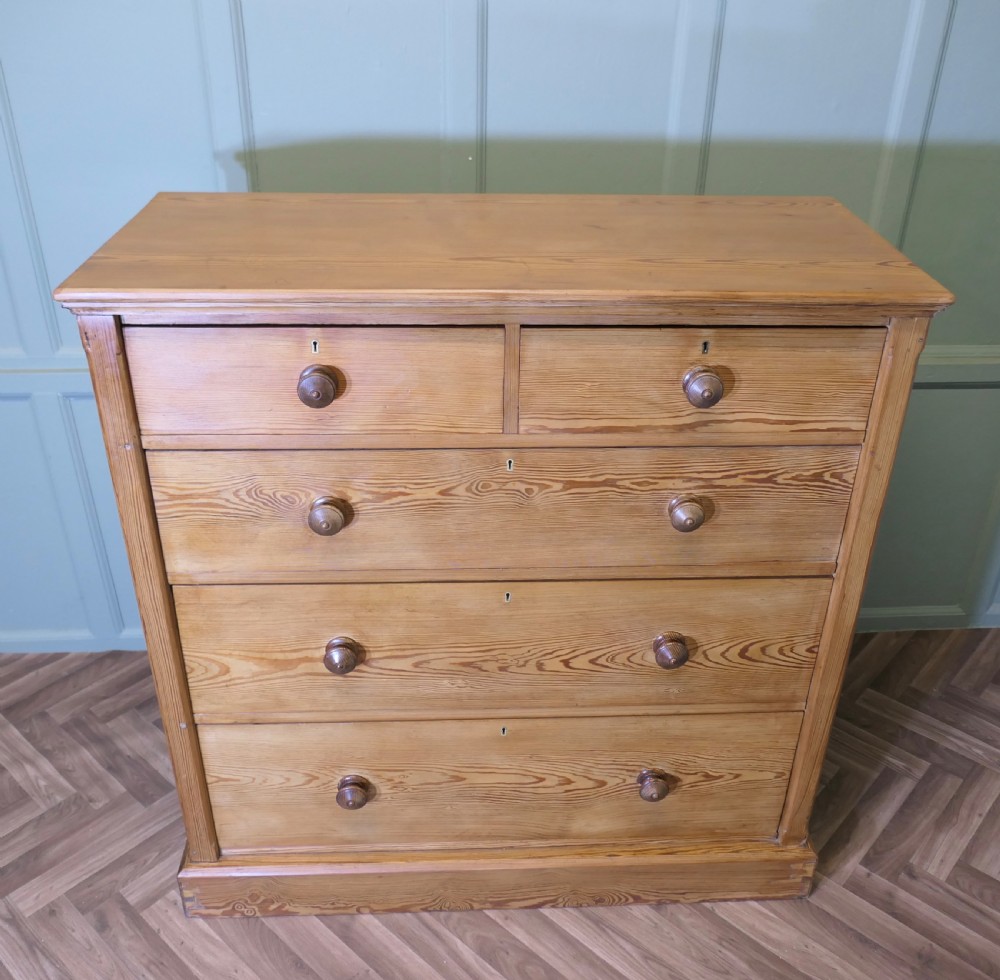 A Victorian stripped pine chest of drawers in a two-over-three arrangement with turned wooden knobs and a solid plinth base.