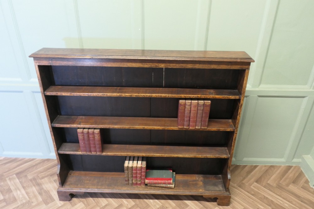 A wide antique dark elm open bookcase featuring four horizontal shelves, a panelled back, and bracket feet. View II