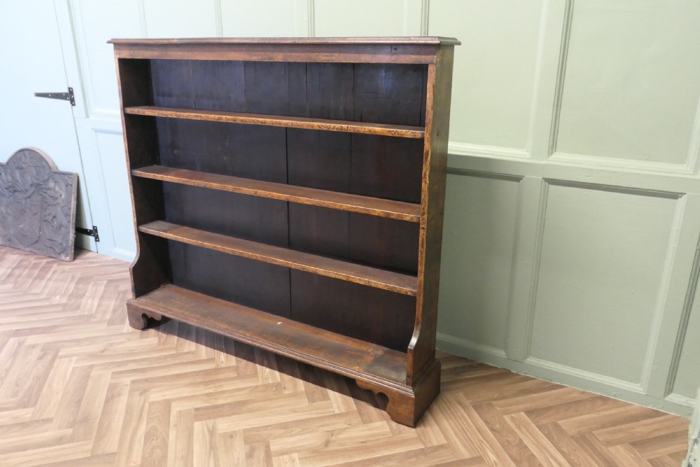 A wide antique dark elm open bookcase featuring four horizontal shelves, a panelled back, and bracket feet. View III