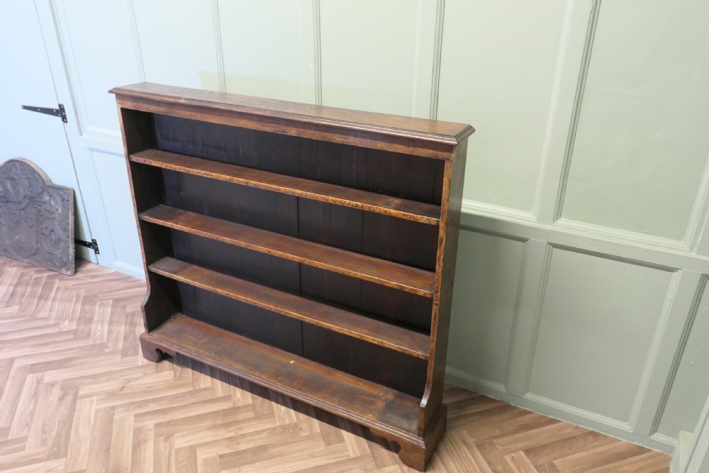 A wide antique dark elm open bookcase featuring four horizontal shelves, a panelled back, and bracket feet. View V