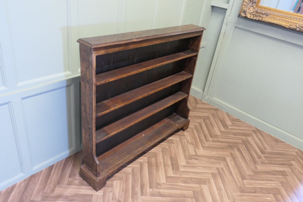 A wide antique dark elm open bookcase featuring four horizontal shelves, a panelled back, and bracket feet. View VI