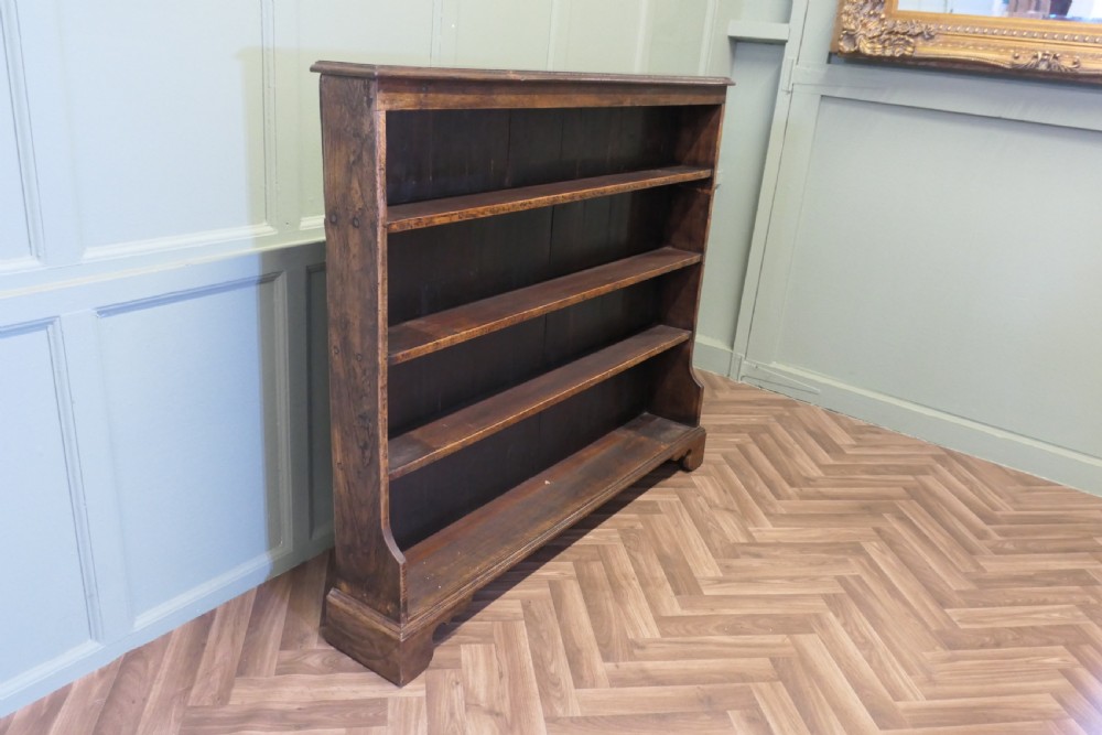 A wide antique dark elm open bookcase featuring four horizontal shelves, a panelled back, and bracket feet. View VII