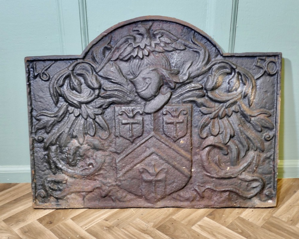 A 17th-century arched cast iron fireback displaying a heraldic crest, a knights helmet with foliage mantling, an eagle, and the date 1650.