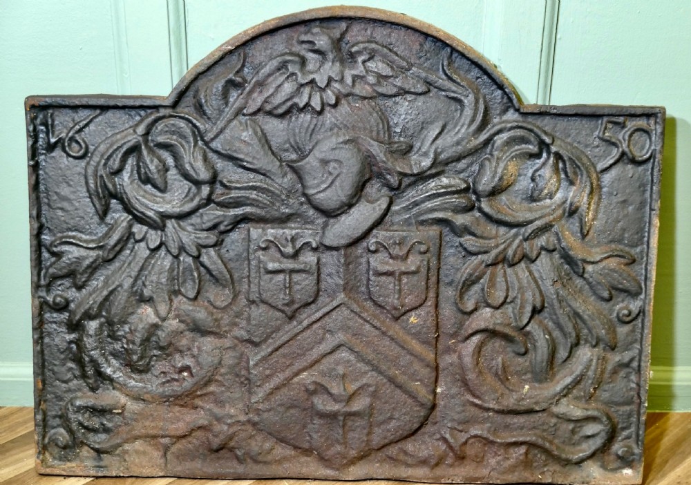 A 17th-century arched cast iron fireback displaying a heraldic crest, a knights helmet with foliage mantling, an eagle, and the date 1650. View III