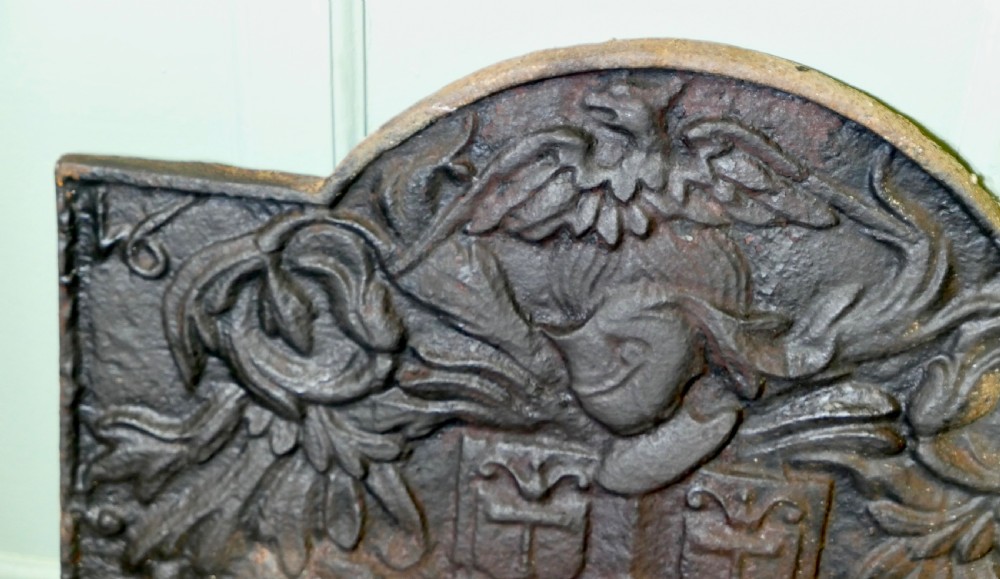 A 17th-century arched cast iron fireback displaying a heraldic crest, a knights helmet with foliage mantling, an eagle, and the date 1650. View IV
