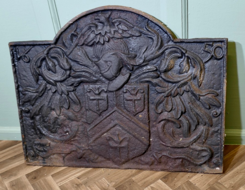 A 17th-century arched cast iron fireback displaying a heraldic crest, a knights helmet with foliage mantling, an eagle, and the date 1650. View VII