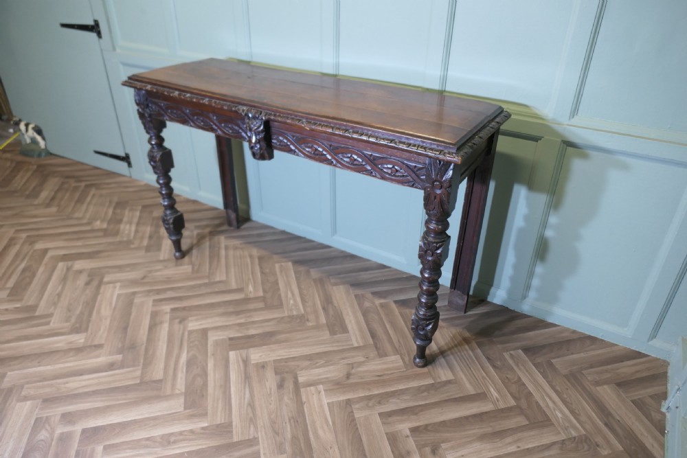 A dark carved oak hall table featuring an intricately carved apron with a central mask motif and turned front legs. View II