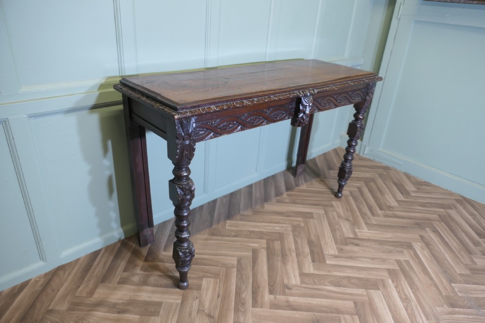 A dark carved oak hall table featuring an intricately carved apron with a central mask motif and turned front legs. View III