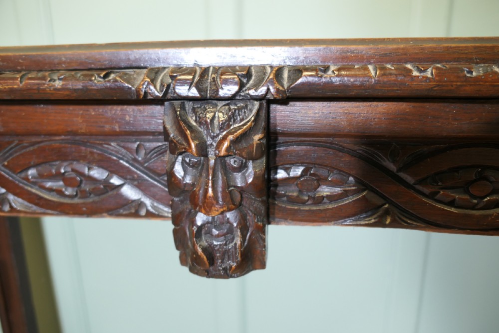 A dark carved oak hall table featuring an intricately carved apron with a central mask motif and turned front legs. View VI