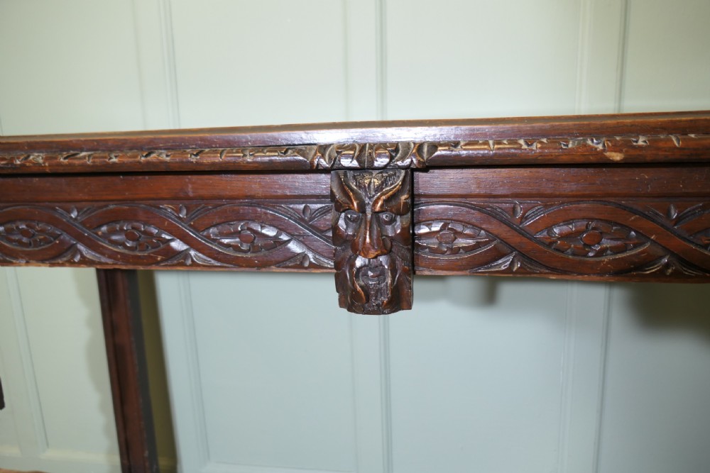 A dark carved oak hall table featuring an intricately carved apron with a central mask motif and turned front legs. View VII
