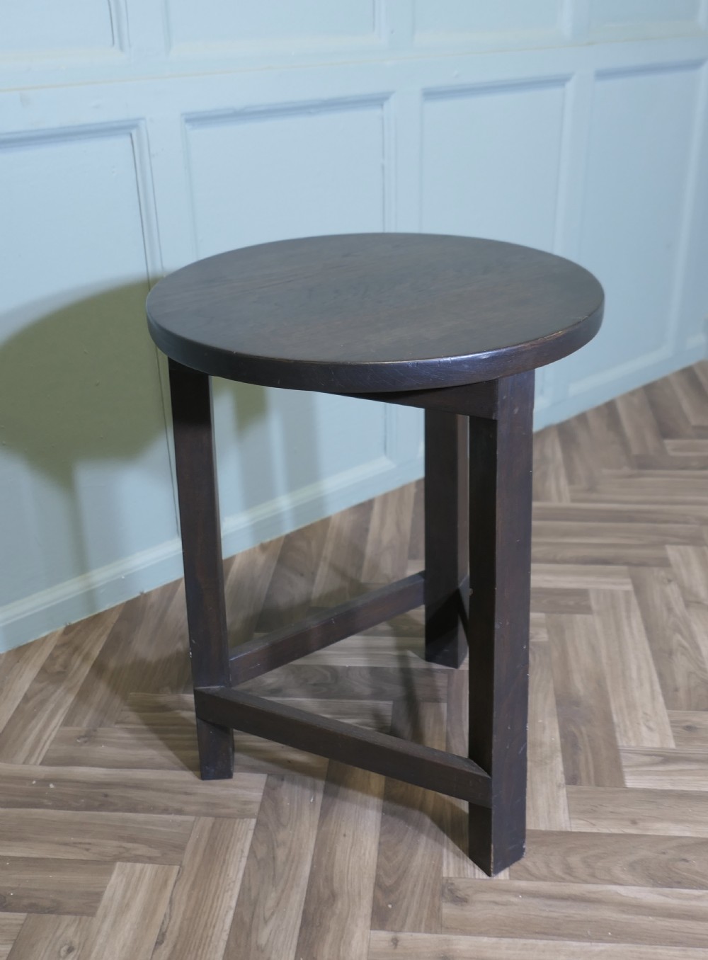 A dark-stained English oak cricket table featuring a circular top supported by three straight legs joined by a lower triangular stretcher. View II