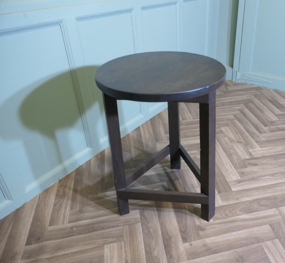 A dark-stained English oak cricket table featuring a circular top supported by three straight legs joined by a lower triangular stretcher. View VI