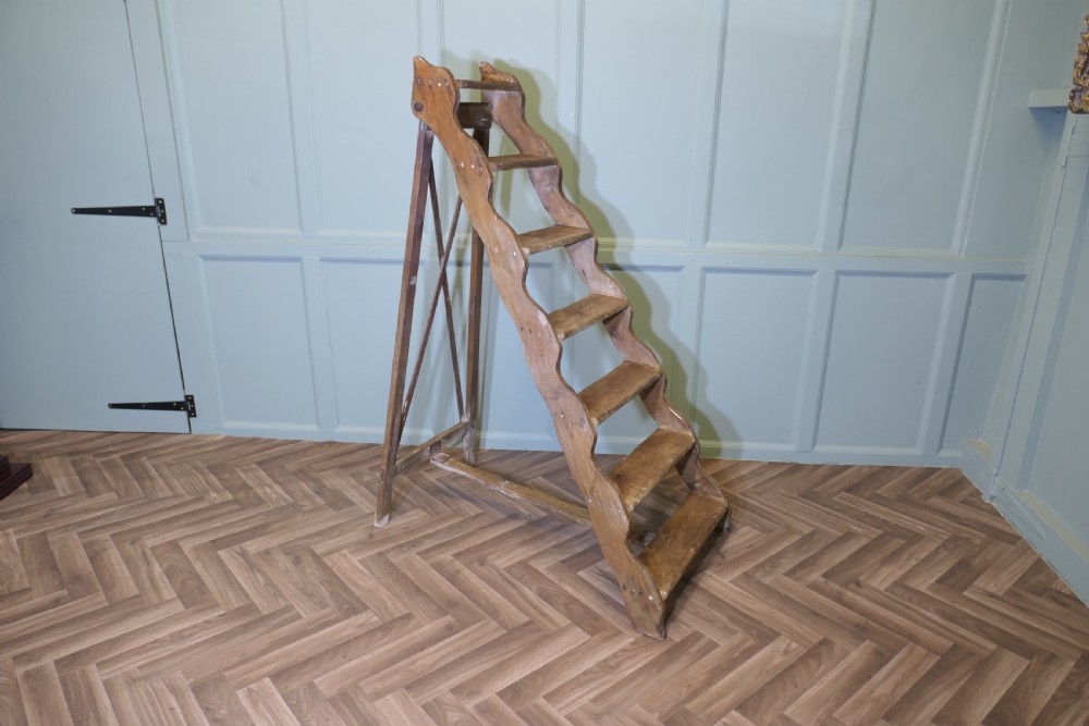 A nineteenth-century folding pine step ladder featuring scalloped wooden side supports and aged timber treads. View II