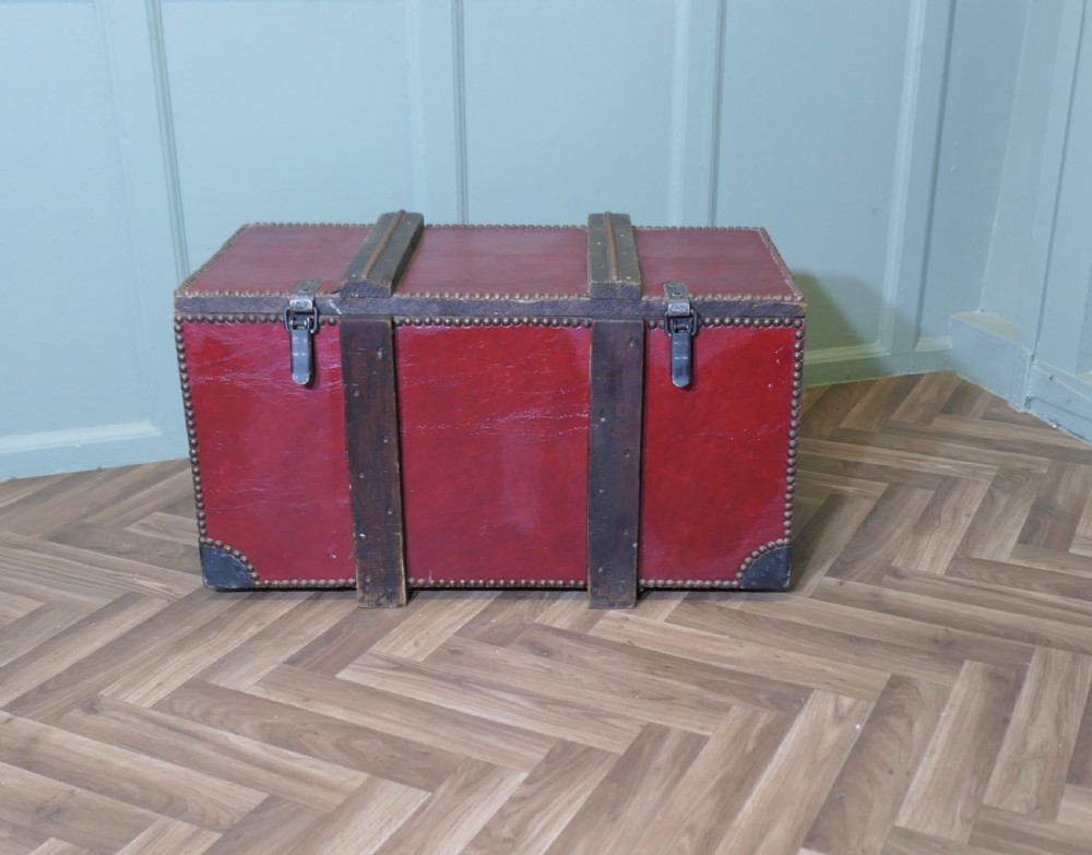 A rectangular dark red leather travel trunk with brass stud trimming, heavy dark wood banding, and iron metal latches resting on a parquet floor. View II