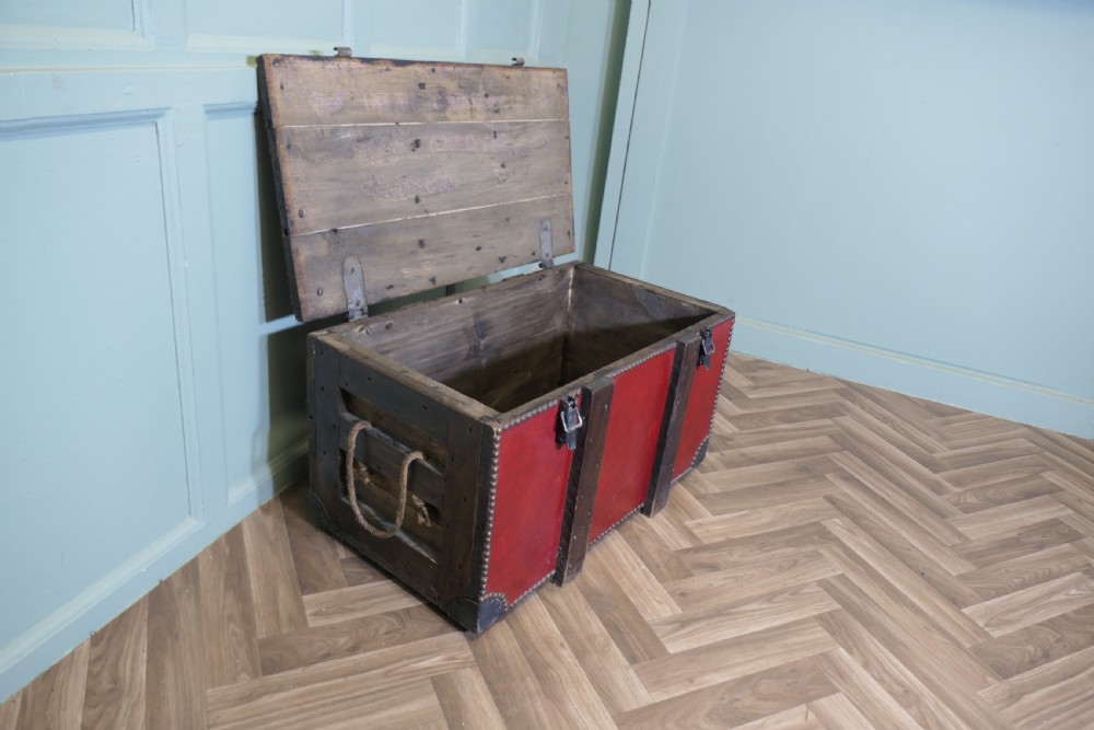 A rectangular dark red leather travel trunk with brass stud trimming, heavy dark wood banding, and iron metal latches resting on a parquet floor. View III
