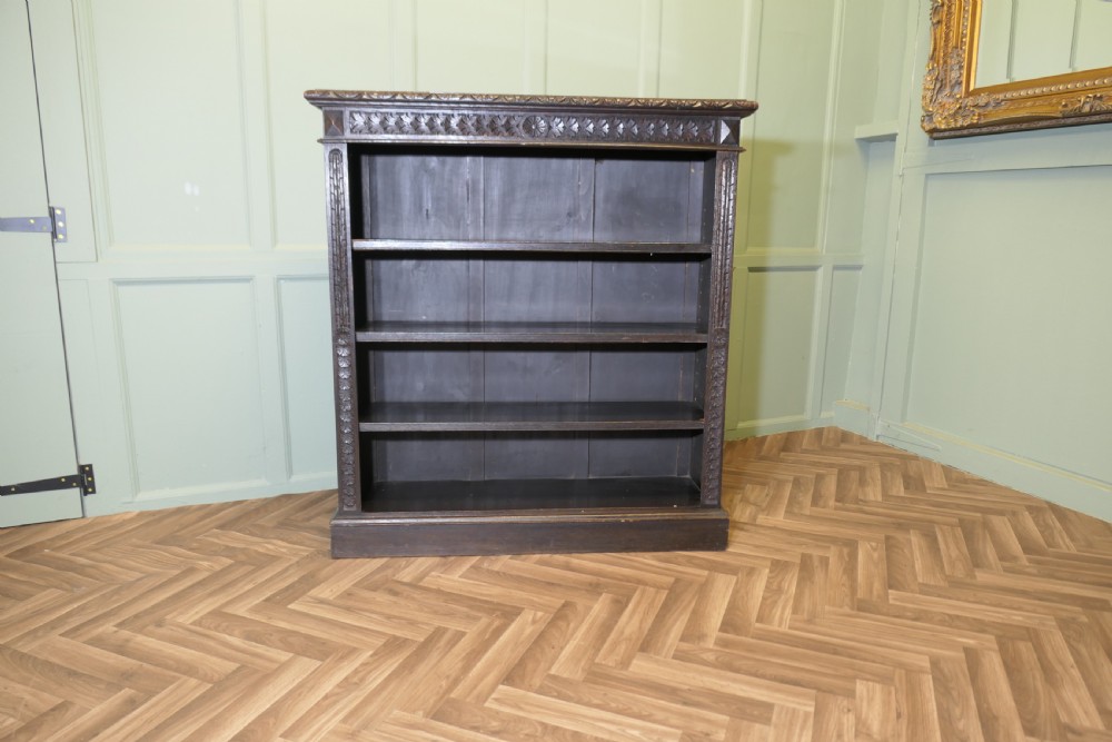 A dark carved oak open bookcase featuring four exposed shelves, a relief carved top frieze, and carved vertical side pilasters. View II