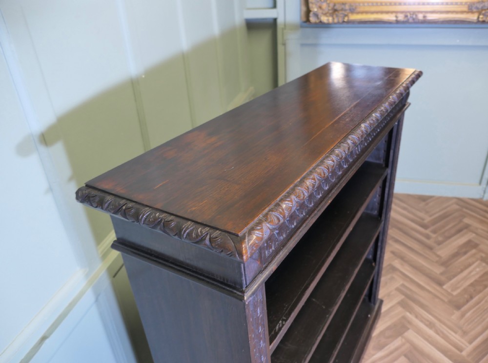 A dark carved oak open bookcase featuring four exposed shelves, a relief carved top frieze, and carved vertical side pilasters. View III