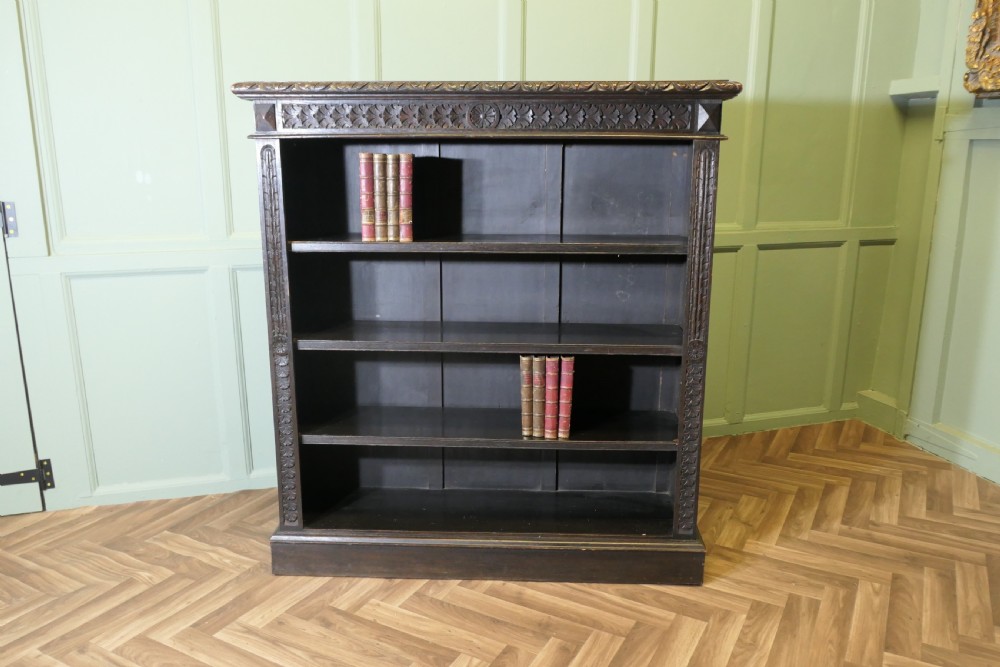A dark carved oak open bookcase featuring four exposed shelves, a relief carved top frieze, and carved vertical side pilasters. View IV