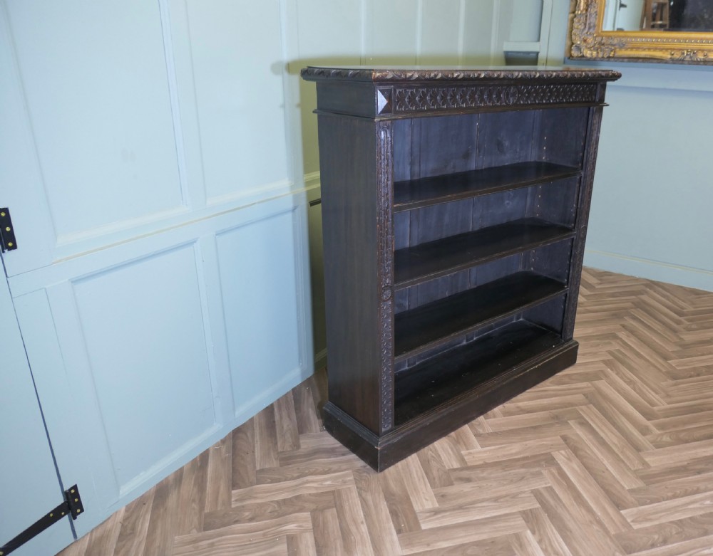 A dark carved oak open bookcase featuring four exposed shelves, a relief carved top frieze, and carved vertical side pilasters. View V