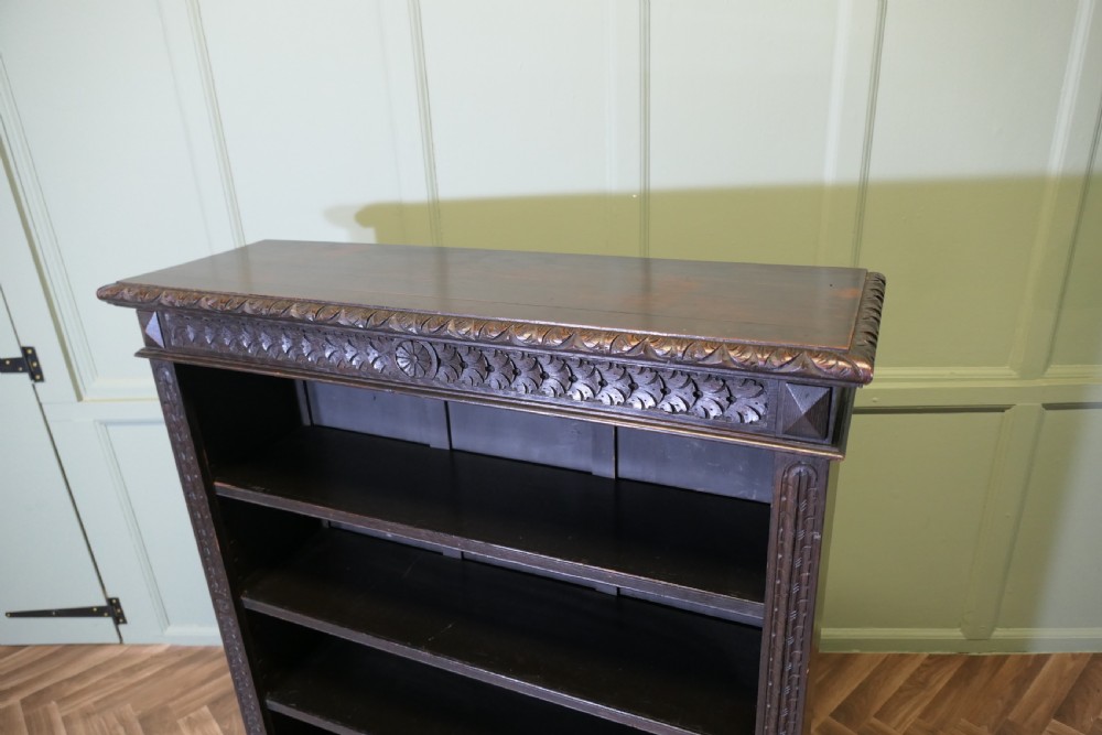 A dark carved oak open bookcase featuring four exposed shelves, a relief carved top frieze, and carved vertical side pilasters. View VI
