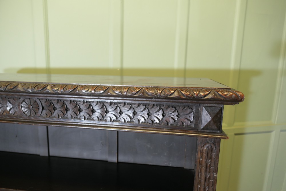 A dark carved oak open bookcase featuring four exposed shelves, a relief carved top frieze, and carved vertical side pilasters. View VII