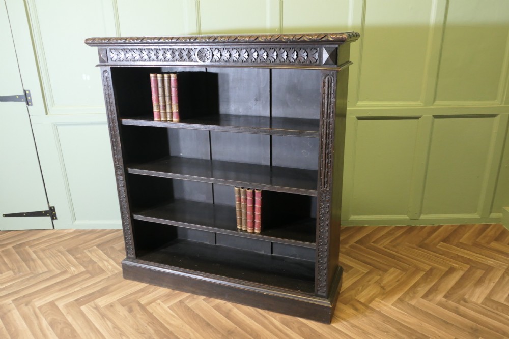 A dark carved oak open bookcase featuring four exposed shelves, a relief carved top frieze, and carved vertical side pilasters. View VIII