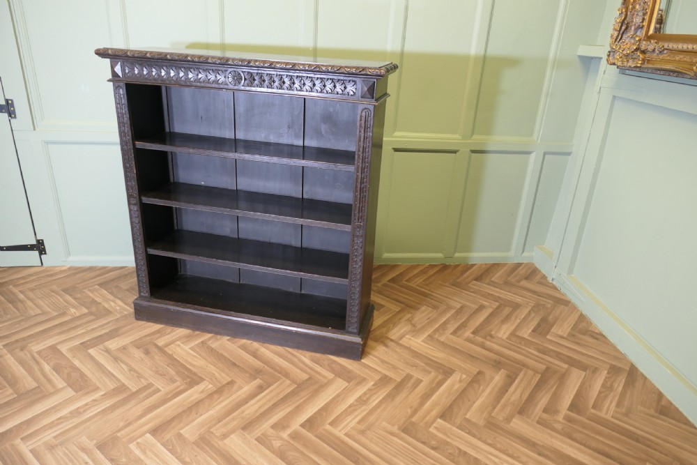 A dark carved oak open bookcase featuring four exposed shelves, a relief carved top frieze, and carved vertical side pilasters. View IX