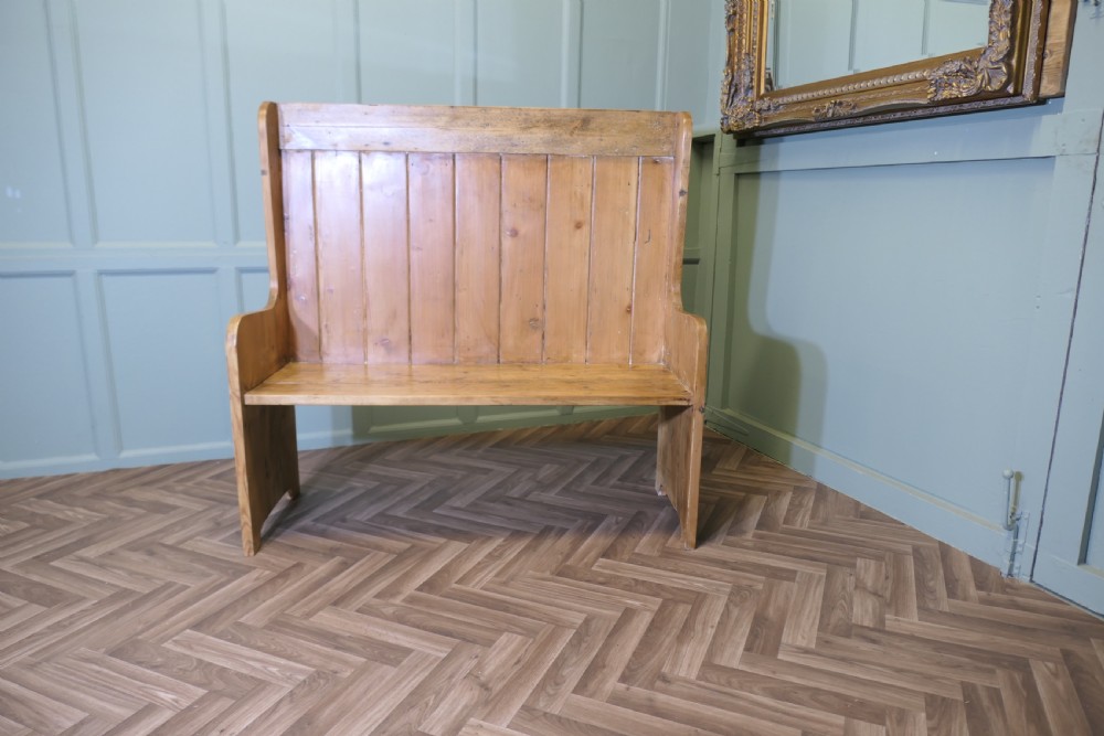 A high-back rustic pine settle bench featuring vertical planking and solid side panels in a natural honey wood finish.