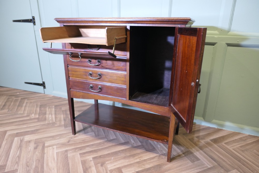 An Edwardian mahogany music cabinet featuring five drop-front drawers on the left, a single cupboard door on the right, brass drop handles, and an open lower shelf. View V