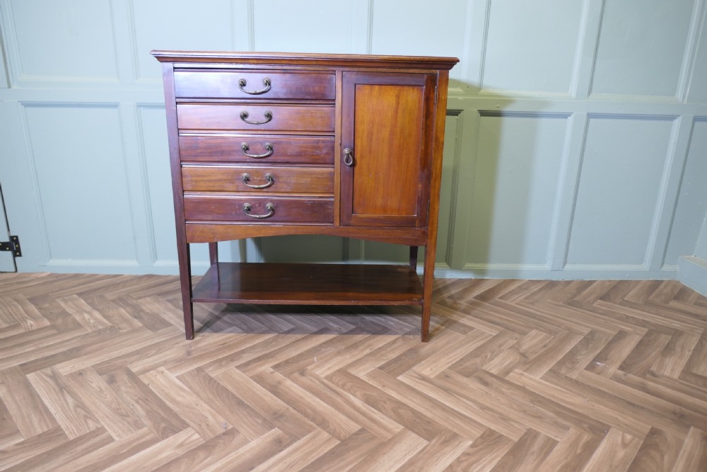 An Edwardian mahogany music cabinet featuring five drop-front drawers on the left, a single cupboard door on the right, brass drop handles, and an open lower shelf.