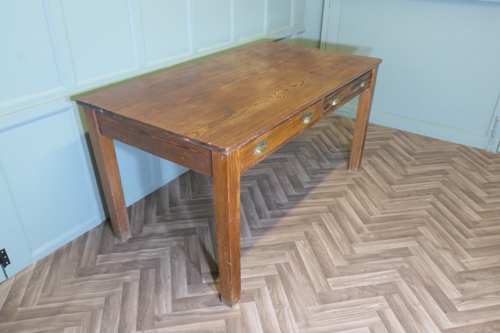 A rectangular antique pine writing table featuring two front drawers fitted with brass cup handles and supported by four straight square legs.
