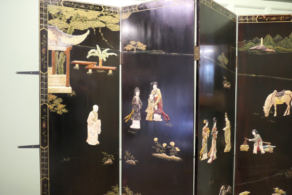 A four-panel black lacquer folding screen decorated with gilt borders and inlaid polychrome relief figures depicting Japanese figures and garden scenery. View II