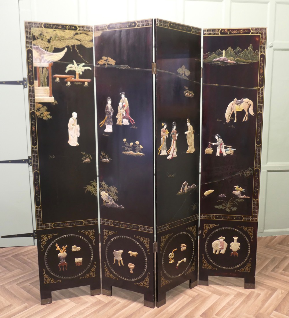 A four-panel black lacquer folding screen decorated with gilt borders and inlaid polychrome relief figures depicting Japanese figures and garden scenery.