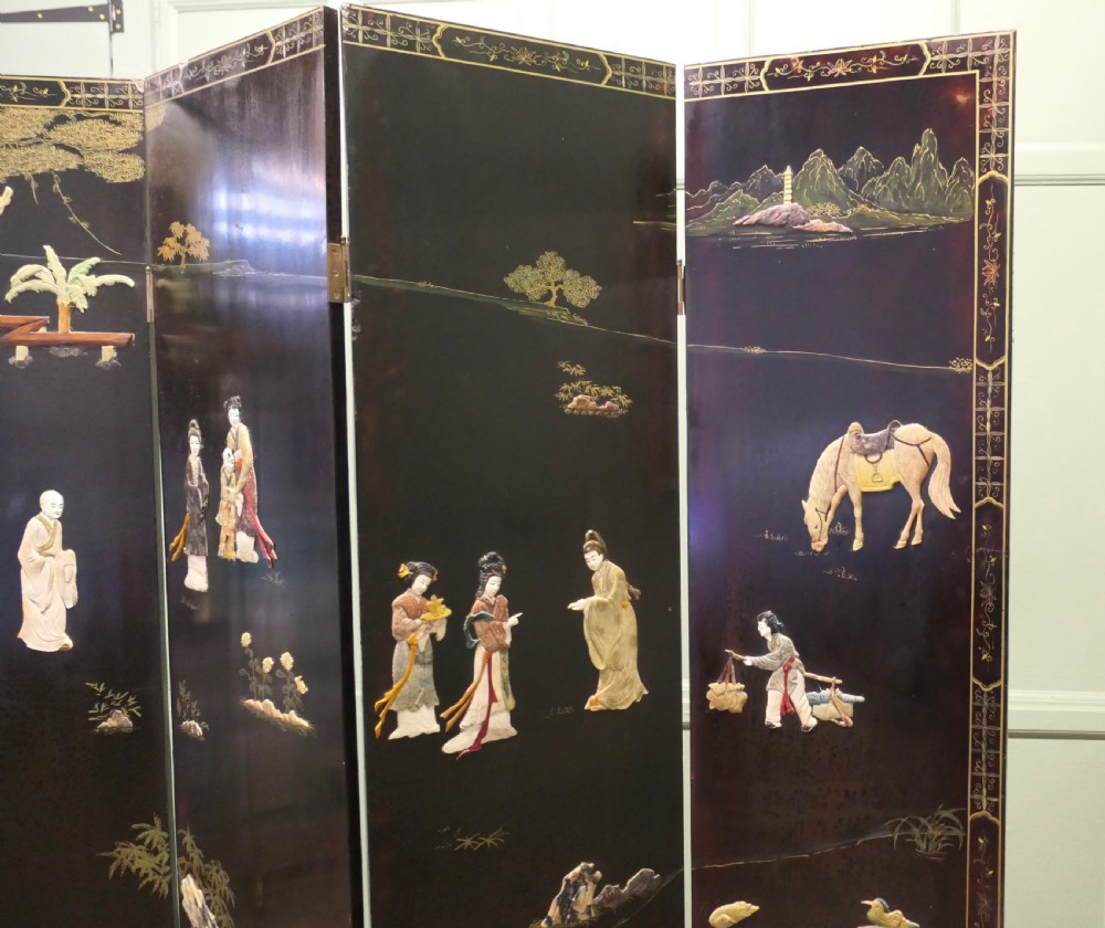 A four-panel black lacquer folding screen decorated with gilt borders and inlaid polychrome relief figures depicting Japanese figures and garden scenery. View V