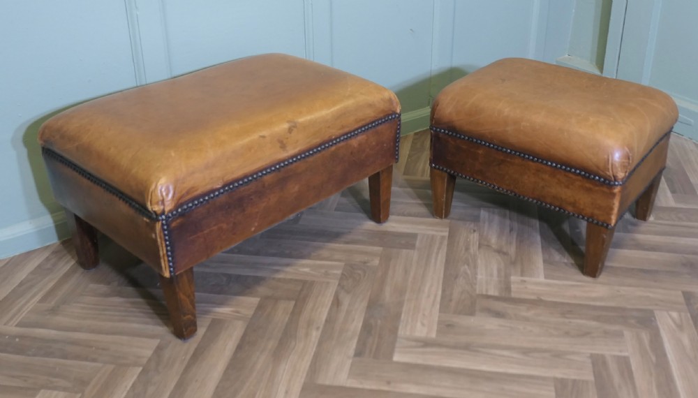 A pair of rectangular tan leather library footstools with close-studded trim detailing on tapered square wood legs.